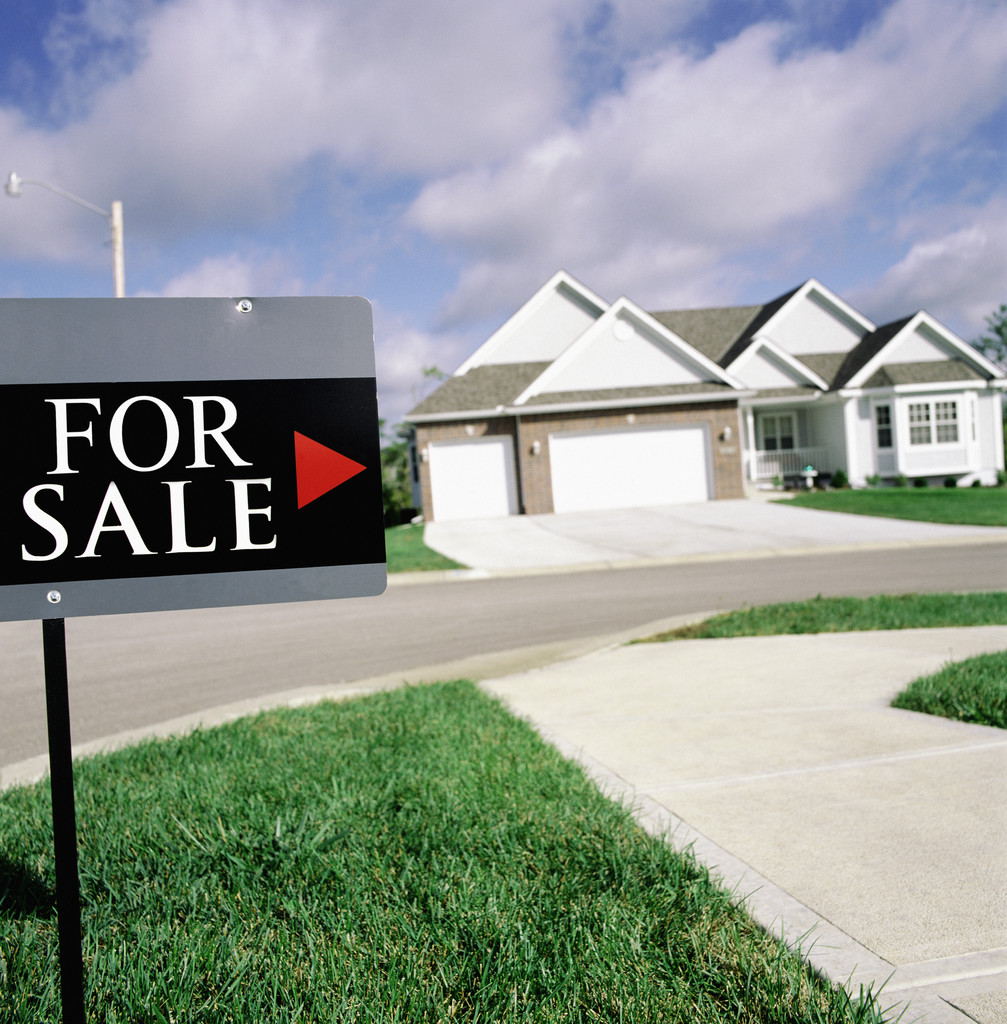 House on suburban street with ‘For Sale’ sign in foreground